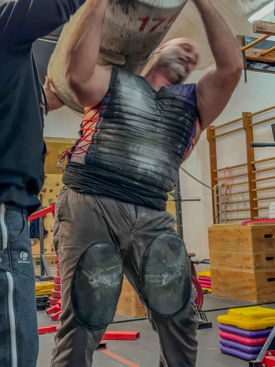 Deportista realizando un levantamiento de piedra vasca con supervisión